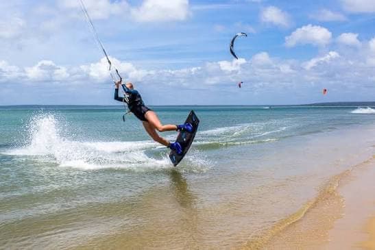 Kitesurfer carving through the shallows, kites in the sky behind
